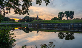 Foto de los alrededores de Naarden, en Holanda Septentrional, Países Bajos, con canal, árboles y atardecer reflejado.
