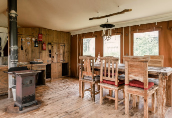 Rustic wood-furnished dining area in Duynlodge - Duynpark, Netherlands, featuring stove and large windows.