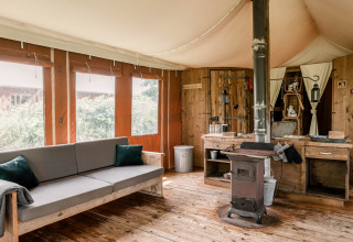 Rustiek lodge-interieur met houtkachel, houten meubilair en grote ramen bij Duynlodge - Duynpark, Nederland.