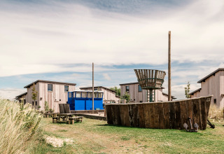 Buitengebied van een lodge met houten chalets, een blauwe bus en speelzone met houten elementen.