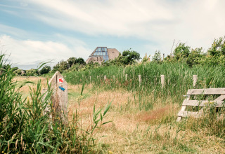 Afbeelding van een lodge achter gras, met houten afsluiting en een wegwijzer onder een bewolkte hemel.