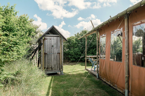 Foto van een houten hutje en lodgetent bij Duynlodge - Duynpark in Nederland, omringd door groen.