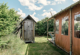 Foto van een houten hutje en lodgetent bij Duynlodge - Duynpark in Nederland, omringd door groen.