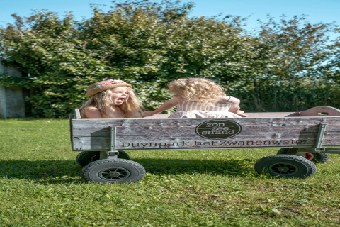 Two children play happily in a wooden cart on the grass at Duynpark het Zwanenwater lodge.