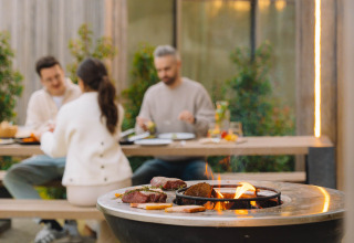 Gegrild vlees op open vuur terwijl drie mensen buiten eten bij Lodge at Woodz Lodges, België.