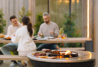 Viande grillée sur un feu de bois, trois personnes dînent en plein air au Lodge at Woodz Lodges, Belgique.