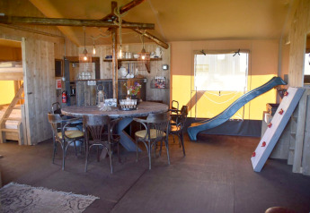 Interno di Kidz Lodge nei Paesi Bassi con tavolo da pranzo, letti a castello, scivolo e parete da arrampicata.