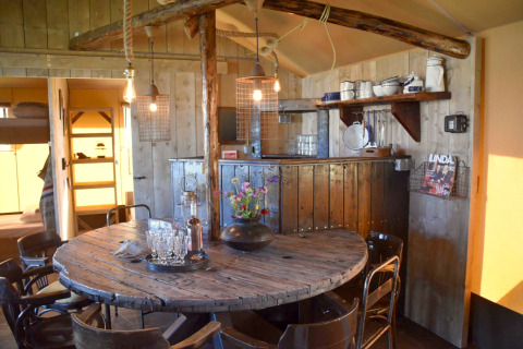 Rustic dining area in Kidz Lodge, Netherlands with wooden round table, chairs and cozy kitchen shelves.