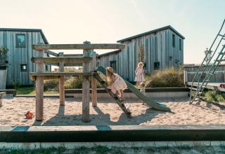 Children play on a playground with sand, wooden climbing frame, and slide at Kidz Lodge in the Netherlands.
