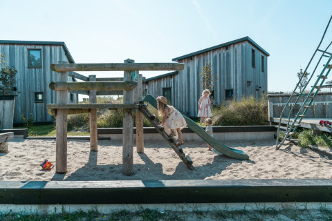 Bambini giocano su un parco giochi con sabbia, scivolo e struttura in legno presso Kidz Lodge nei Paesi Bassi.