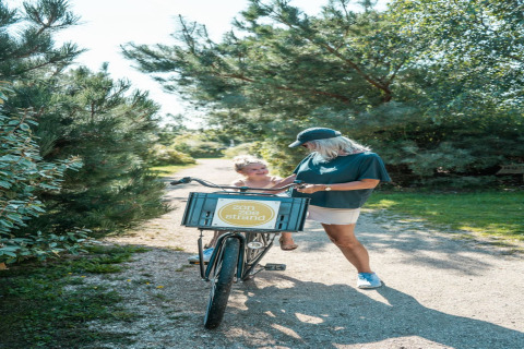 Donna e bambino si godono una giornata di sole con una bicicletta su un sentiero di un lodge tra alberi.