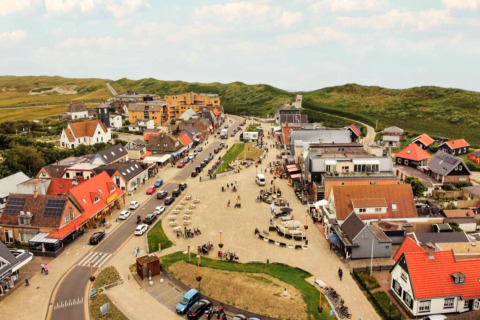 Aerial view of a charming village with colorful rooftops and green hills in the background by a lodge.