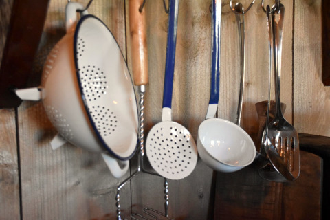 Kitchen utensils including colander, ladle, and slotted spoon hanging on a wooden wall at Kidz Lodge, Netherlands.