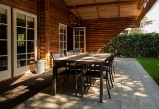 Udendørs spiseplads ved træhytte, Paalchalet 723, Belgien, med bord, stole og grøn hæk.