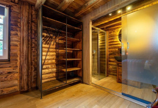 Interiør af en træhytte med et åbent garderobeskab, badeværelse med glasdør og trævægge, Paalchalet 723.