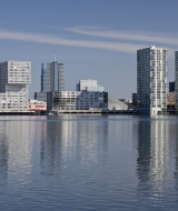 Horizonte moderno de Almere, Flevolanda, Países Bajos, con altos edificios reflejados en el agua azul.
