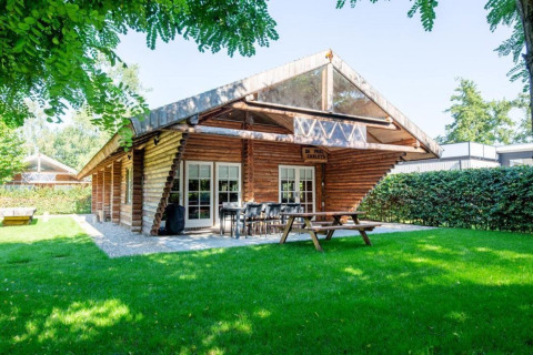Træhytte på grøn græsplæne ved navn Paalchalet 723 med udendørs siddepladser og frodige omgivelser.
