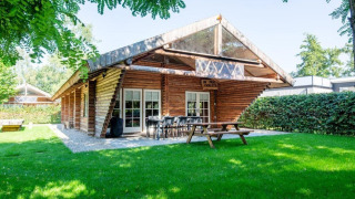 Blockhütte Paalchalet 723 mit Garten, Holztisch und Stühlen im Freien, umgeben von Bäumen und Hecken.