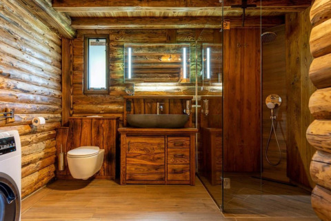 Rustikt badeværelse i træ i Paalchalet 723, Belgien, med brusekabine, håndvask og moderne toilet.