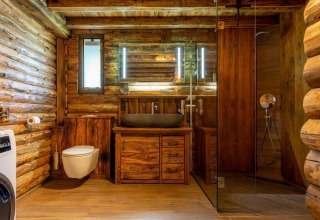 Rustikt badeværelse i træ i Paalchalet 723, Belgien, med brusekabine, håndvask og moderne toilet.