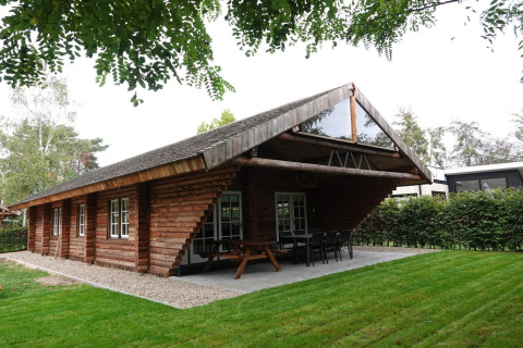 Et træhytte kaldet Paalchalet 723 med store vinduer og terrasse i grønne omgivelser i Belgien.