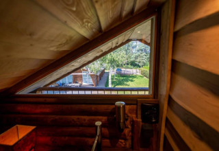 Udsigt fra et trekantet vindue i træindretning på Paalchalet 723-lodgen, med have og træer udenfor.