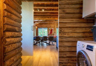 Interiør af bjælkehytte med trævægge, vaskemaskine og udsigt til spisebord, Paalchalet 723, Belgien.