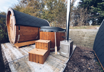 Pod glamping all'aperto con sauna in legno e vasca idromassaggio da REBL Outdoor nei Paesi Bassi, immerso nella natura.