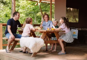 Family enjoys time at a picnic table outside a safari tent, Veluwe Lodge, at Camping Samoza in the Netherlands.