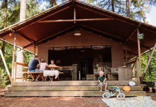 Famiglia si rilassa davanti alla tenda safari Veluwe Lodge al Camping Samoza nei Paesi Bassi, tra gli alberi.