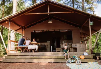 Famiglia si rilassa davanti alla tenda safari Veluwe Lodge al Camping Samoza nei Paesi Bassi, tra gli alberi.