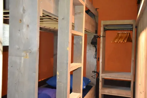 Interno di una tenda lodge safari al Camping Samoza con letti a castello e armadio aperto in legno.