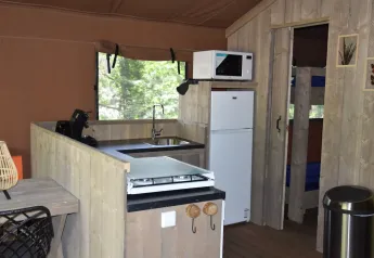 Área de cocina dentro de una tienda Veluwe Lodge en Camping Samoza, con estufa, fregadero, nevera y microondas.