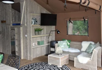 Interior de una tienda safari Veluwe Lodge en Camping Samoza, Países Bajos, con muebles de madera clara.