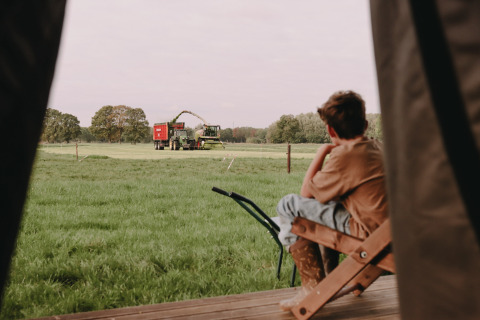 Boy sits on porch and looks out over a field with farm machinery near Valkenswaard, North Brabant, Netherlands.