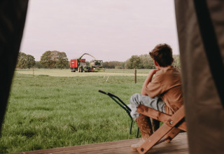 Boy sits on porch and looks out over a field with farm machinery near Valkenswaard, North Brabant, Netherlands.