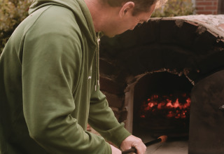 Man in green hoodie cooking by wood-fired oven at Feather Down De Oude Melkstal, North-Brabant, Netherlands.