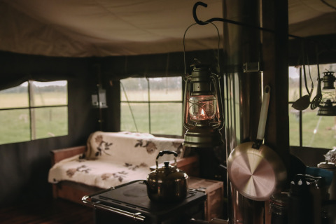 Gezellig tentinterieur met lamp, fornuis, zetel en uitzicht op het platteland bij Feather Down De Oude Melkstal.