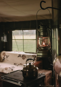 Intérieur de tente douillet avec lanterne, poêle, canapé et vue sur la campagne à Feather Down De Oude Melkstal.