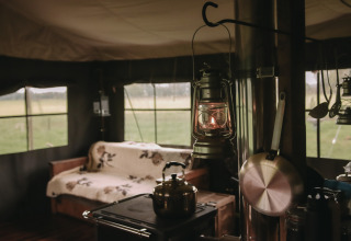 Gezellig tentinterieur met lamp, fornuis, zetel en uitzicht op het platteland bij Feather Down De Oude Melkstal.