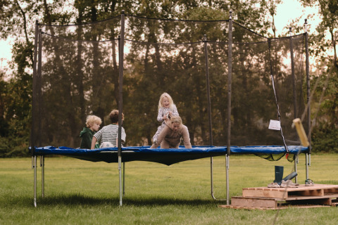 Børn og voksen leger på en trampolin i en grøn park ved Feather Down De Oude Melkstal, Nord-Brabant.