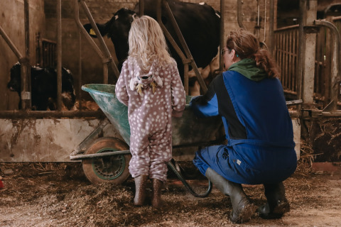 Een volwassene en een kind in dierenpak werken samen in een stal met koeien in De Oude Melkstal.