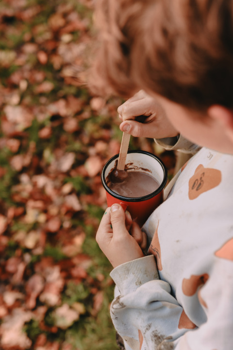 Un bambino mescola una cioccolata calda in una tazza rossa, tra foglie autunnali vicino a Valkenswaard.