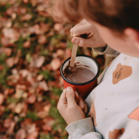 Un enfant mélange du chocolat chaud dans une tasse rouge, entouré de feuilles d’automne près de Valkenswaard.