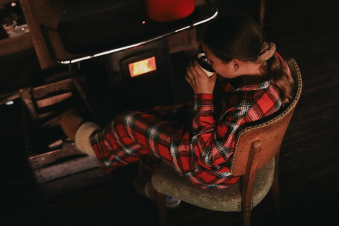 Girl in plaid pajamas sipping a hot drink by a stove at Feather Down De Oude Melkstal, North-Brabant, Netherlands.
