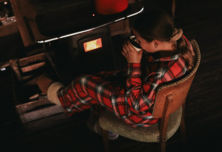 Girl in plaid pajamas sipping a hot drink by a stove at Feather Down De Oude Melkstal, North-Brabant, Netherlands.