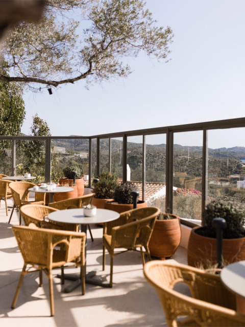 Outdoor terrace with wicker chairs and round tables, hillside views at Wecamp Cadaqués in Catalonia, Spain.