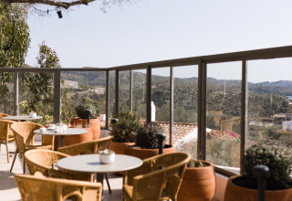 Außenterrasse mit Korbstühlen und runden Tischen, Blick auf Hügel bei Wecamp Cadaqués in Katalonien.