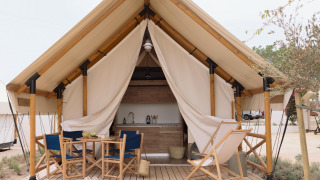 Safari telt Glamping Family Plus med træterrasse, stole, bord og synligt køkken i naturskønne omgivelser.