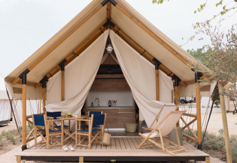 Tenda safari Glamping Family Plus con veranda in legno, sedie, tavolo e cucina a vista in ambiente naturale.